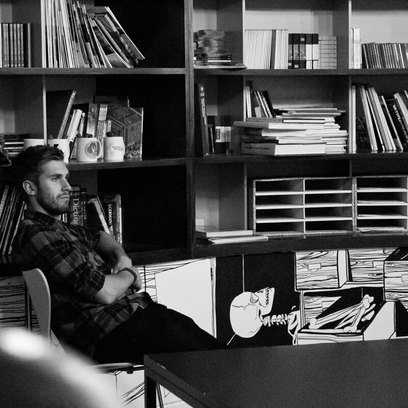 black and white photo of a man sat next to a book shelf